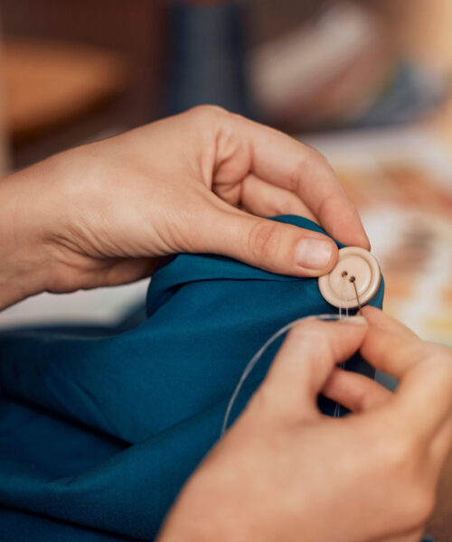Womab, hands and sewing clothes button in studio for designer wear, fashion garment and creative fa.
